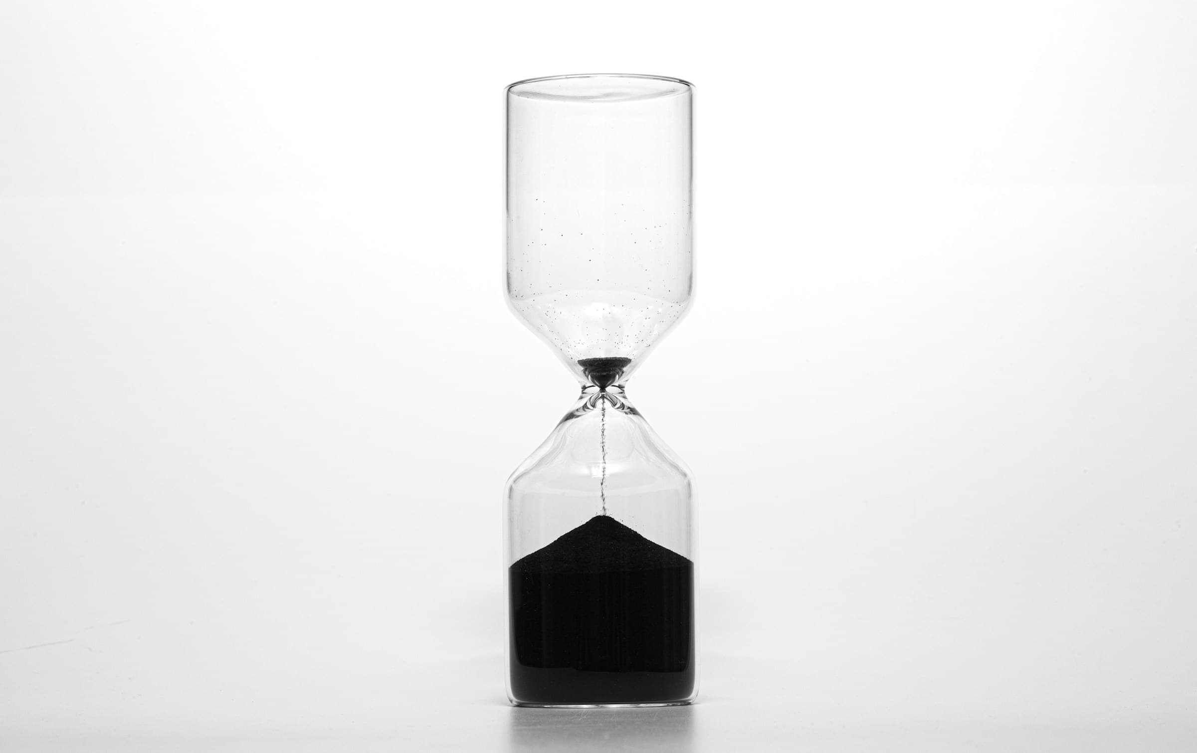An hourglass with the last dark sand running into the lower glass